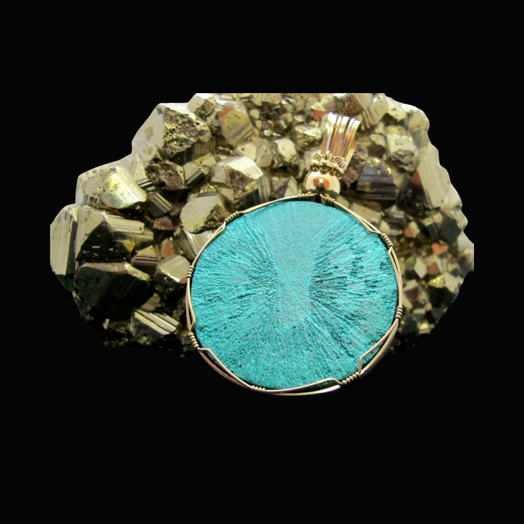 A silver wire-wrapped pendant with a round turquoise-colored textured stone, placed on a bed of metallic mineral crystals against a black background.