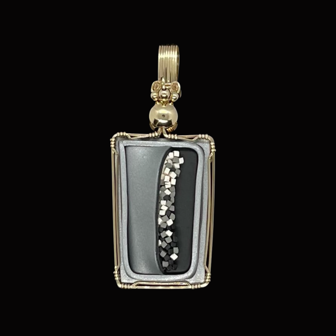 Gold pendant with a rectangular frame, black and gray interior, featuring a curved row of small metallic beads and embedded crystals, on a black background.