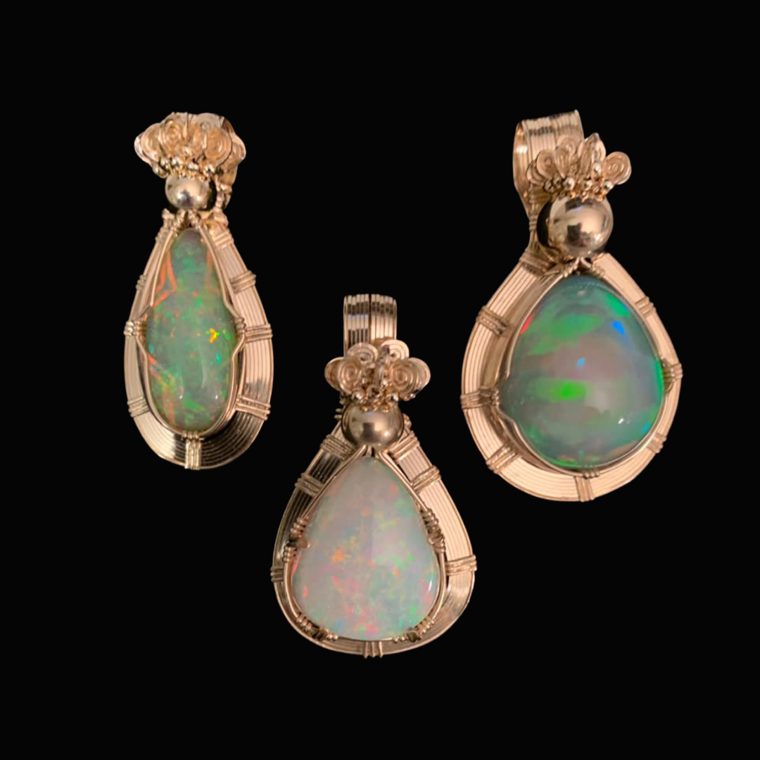 Set of three opal jewelry pieces, including two pendants and one ring, with silver settings and floral accents, displayed on a black background.