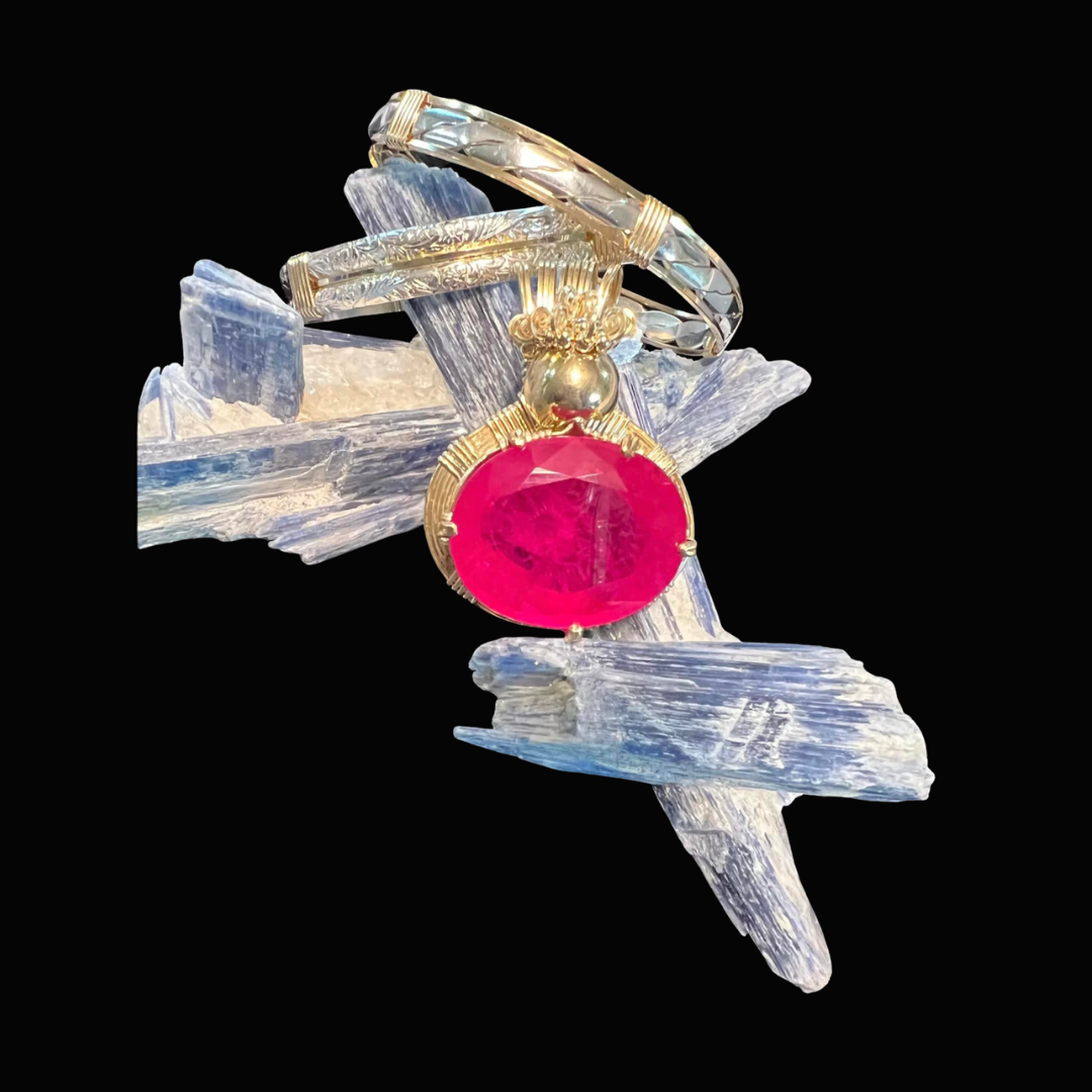 A jewelry piece with a large pink gemstone set in gold, placed on a background of blue ice-like crystals with a black backdrop.