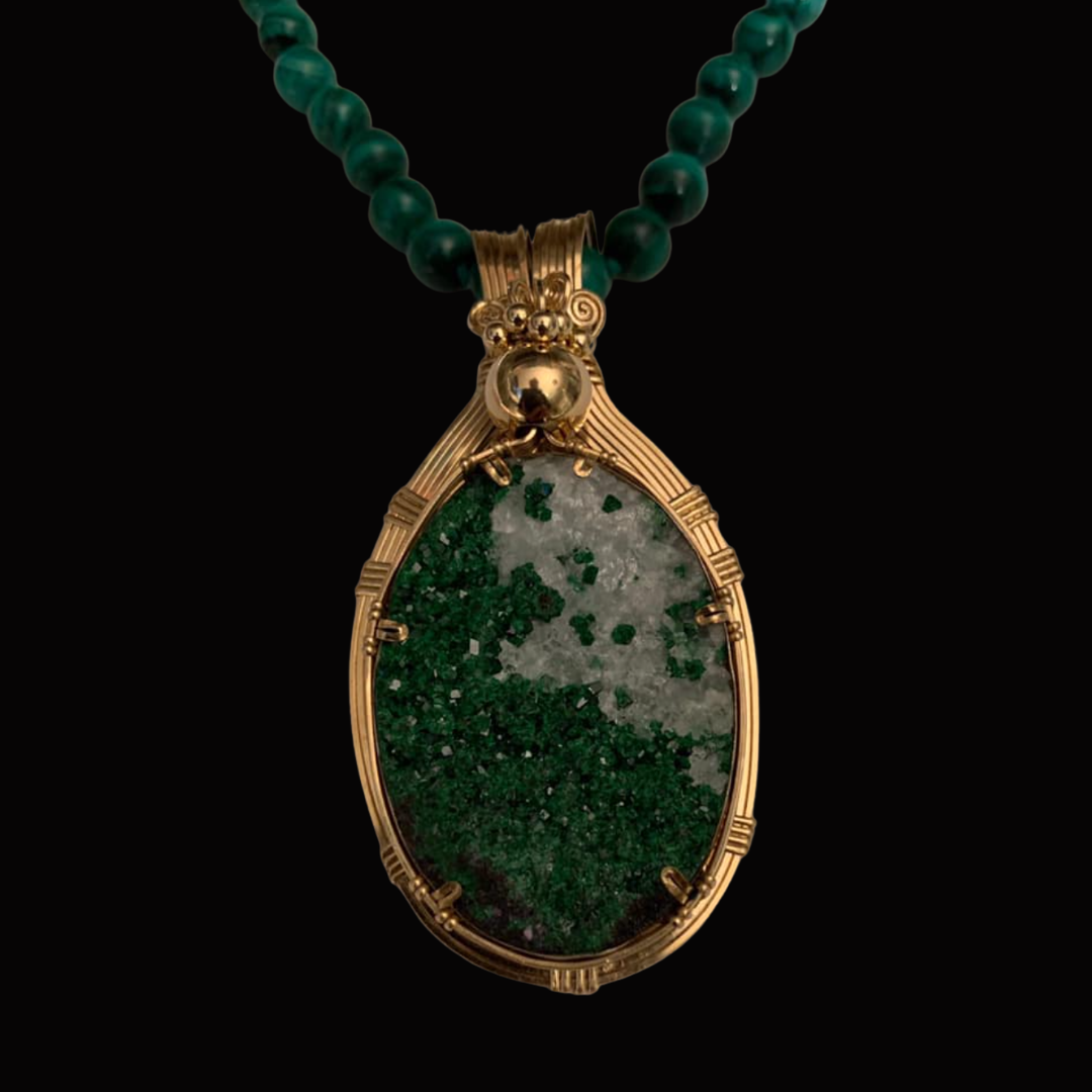 Close-up of a gold pendant with a large, oval green and gray mineral and a beaded green necklace against a black background.