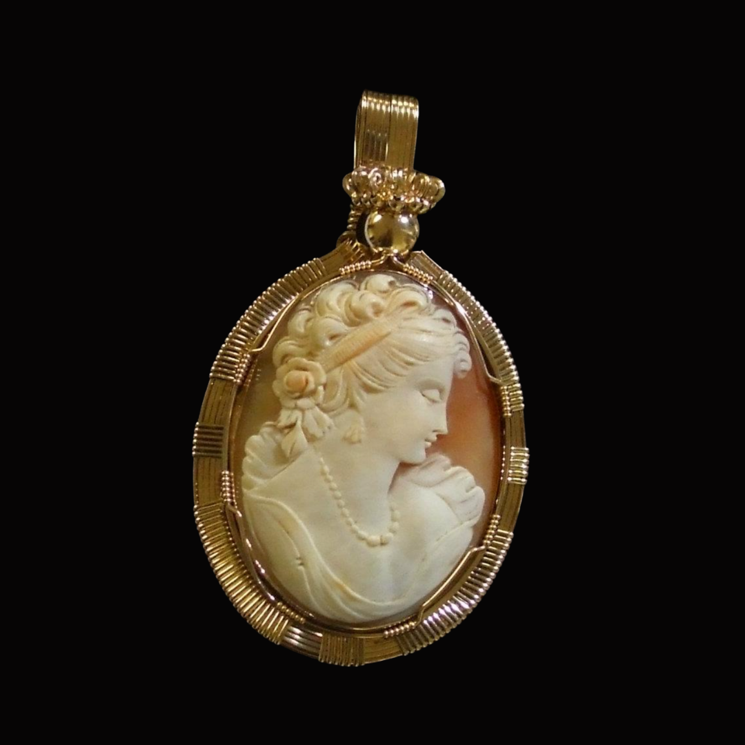 Gold pendant with an intricate carved cameo of a woman with curly hair, adorned with a beaded necklace, set in a detailed gold frame against a black background.