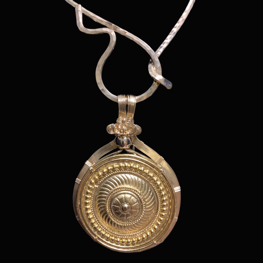 Gold pendant with intricate circular design, hanging from a silver chain against a black background.