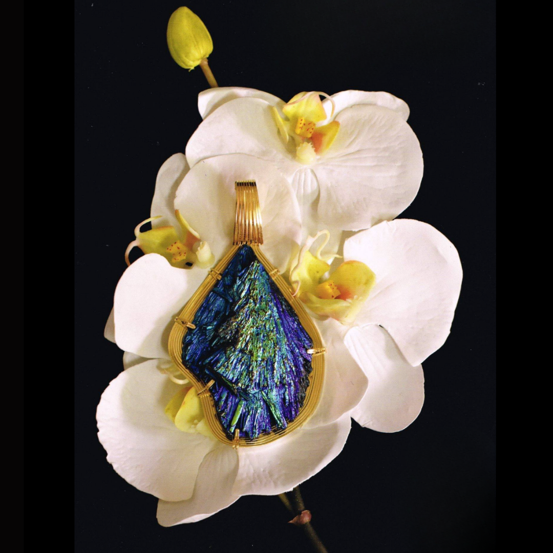 A decorative jewelry piece with a butterfly design made of iridescent glass, resting on white orchid flowers against a black background.