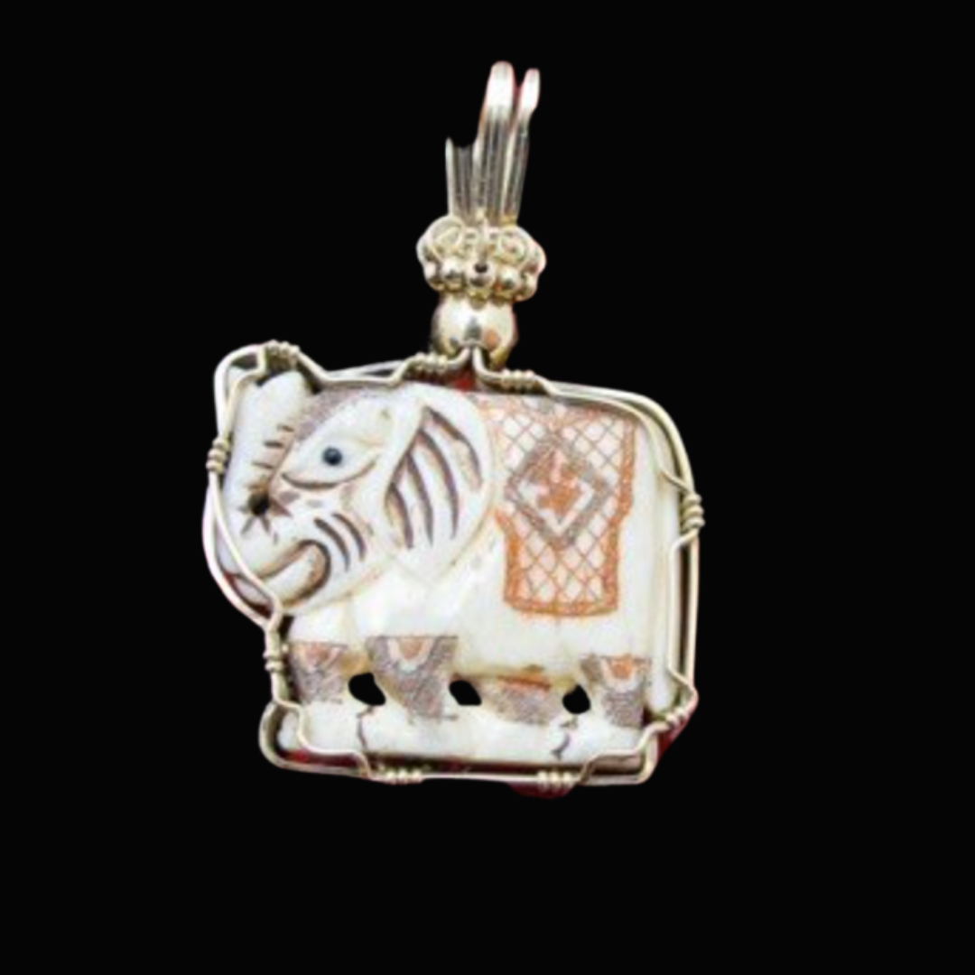 Silver pendant with a carved elephant design, decorated with intricate patterns, set against a black background.