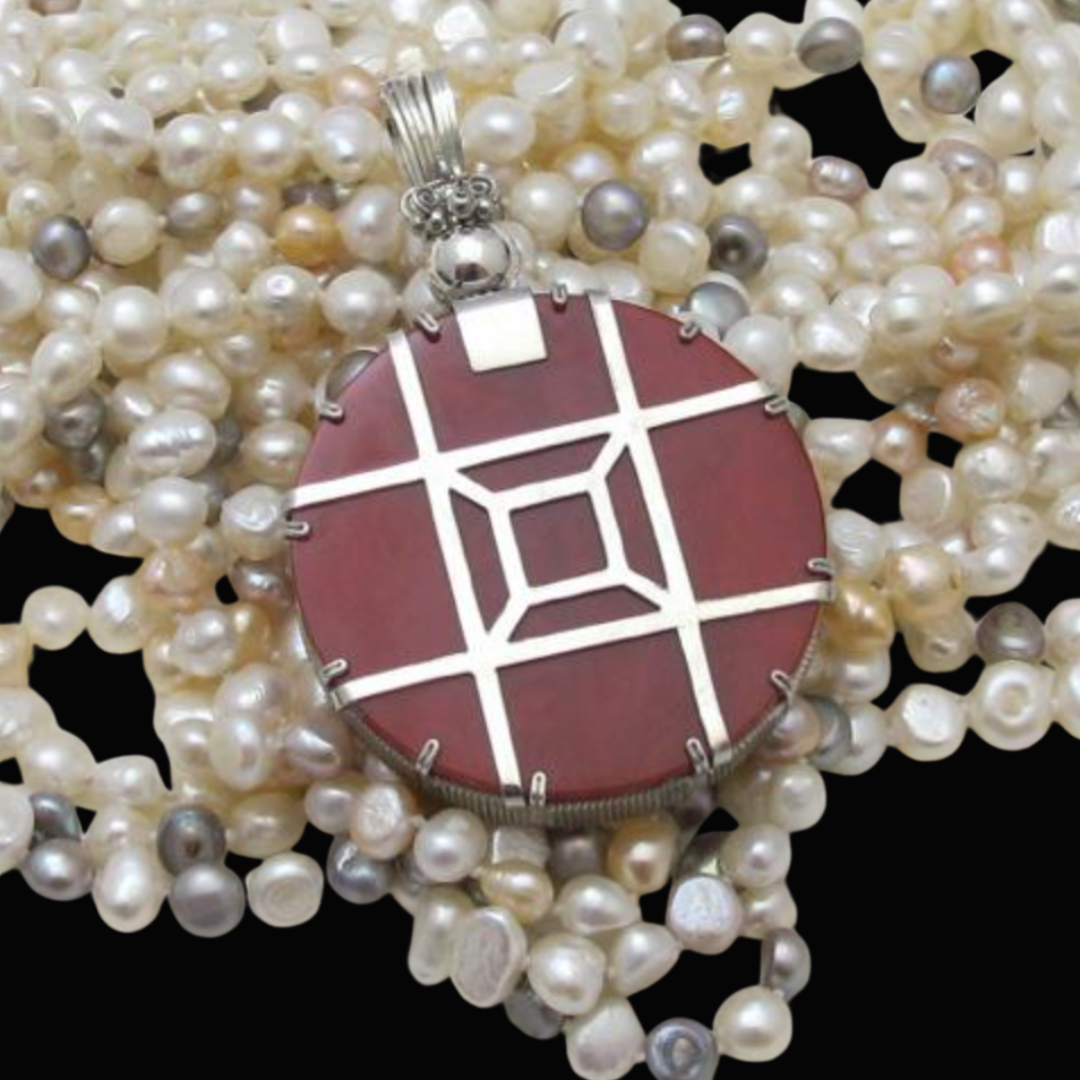 A pendant with geometric design resting on a string of pearls.