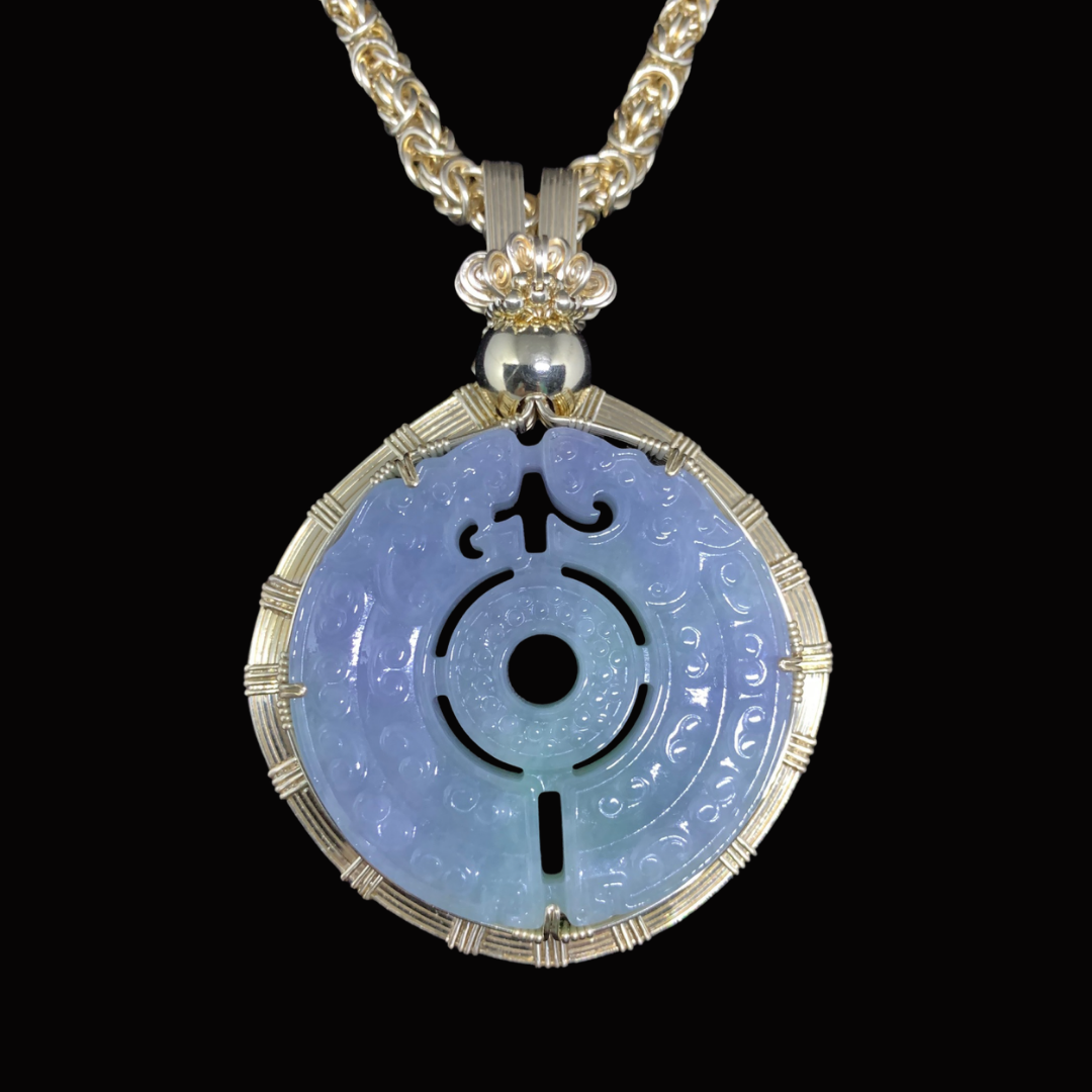 A circular jade pendant with intricate engravings, set in a decorative gold frame, hanging from a thick gold chain with a textured pattern, against a black background.