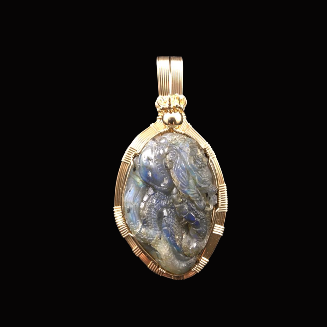 Gold pendant with an iridescent carved stone resembling a dragon or mythical creature against a black background.