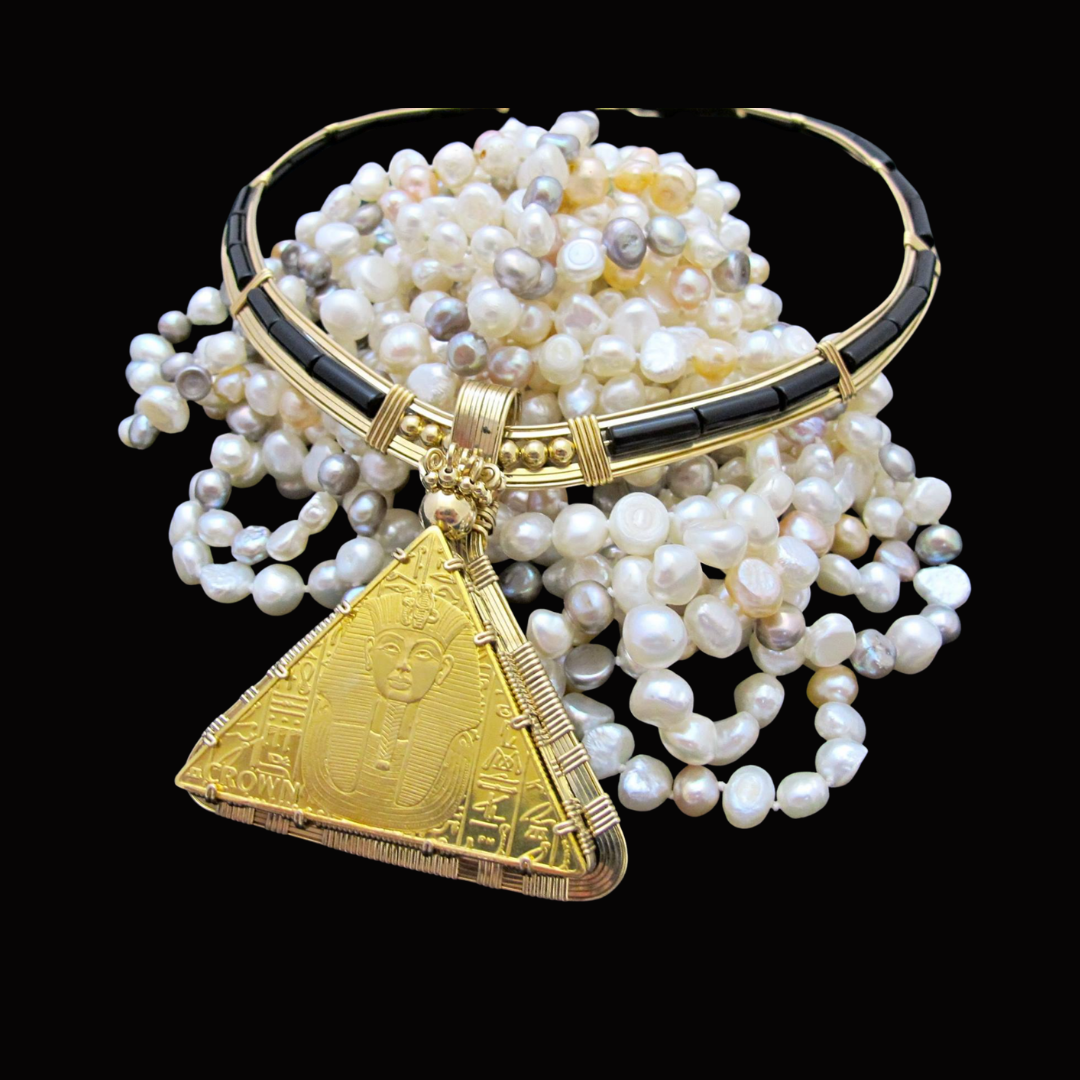 Collection of pearl necklaces with a prominent Egyptian golden pyramid pendant against a black background.