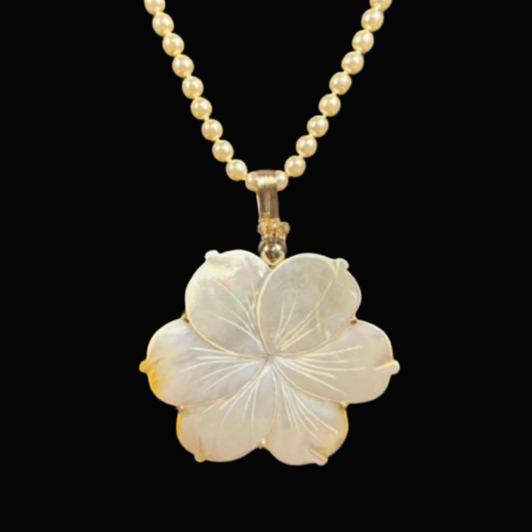A pearl necklace with a large mother-of-pearl flower pendant on a black background.