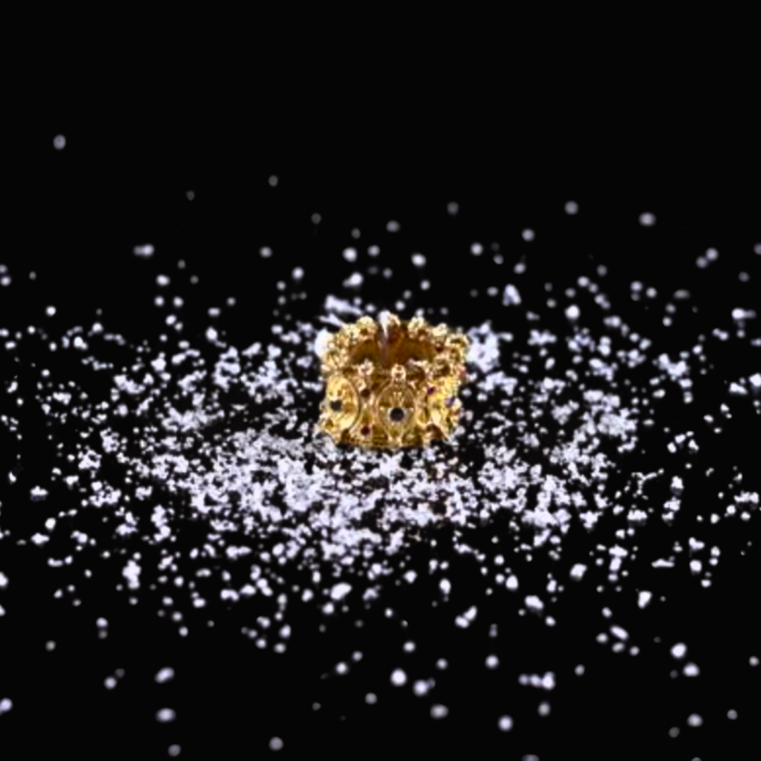 Close-up of a small, intricate gold ring surrounded by scattered white particles on a black background.