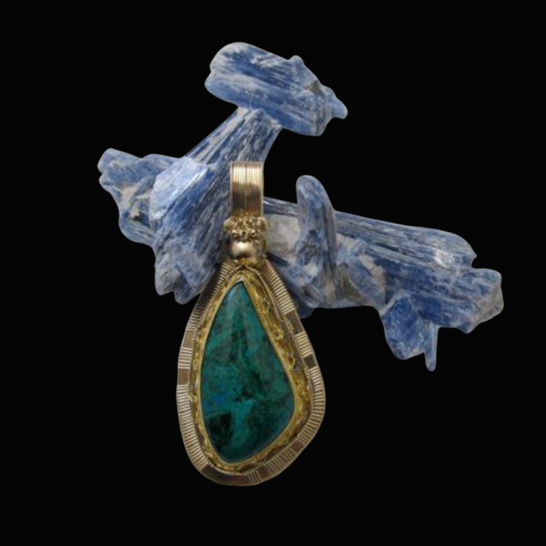 A pendant with a large green gemstone surrounded by a gold and silver frame, hanging on a piece of blue and white marbled stone shaped like a branch or leaf.