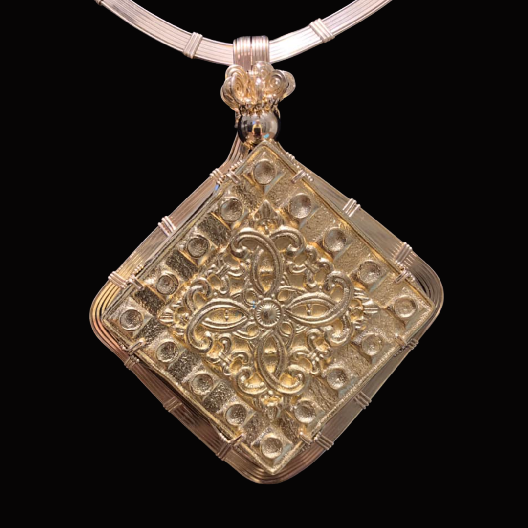 A silver and gold ornate square pendant necklace with a floral design on a white cord against a black background.
