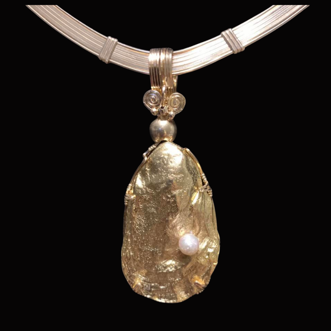 A gold necklace with a large, textured gold pendant and a small white pearl, set against a black background.