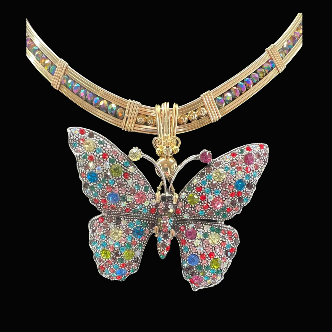 Colorful butterfly-shaped pendant with glittering multicolored stones hanging from a gold and multicolored beaded necklace against a black background.
