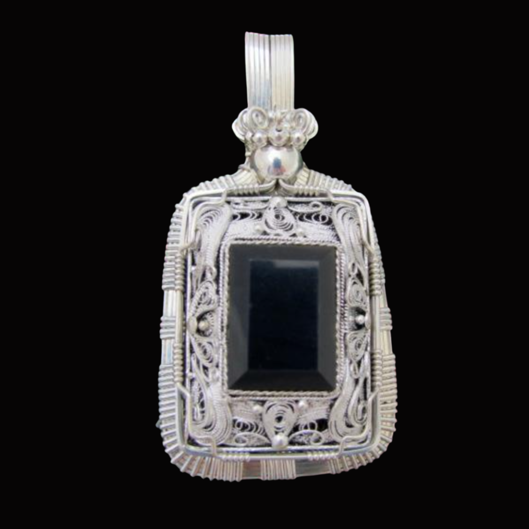 Silver pendant with intricate filigree design and a rectangular black stone in the center, set against a black background.