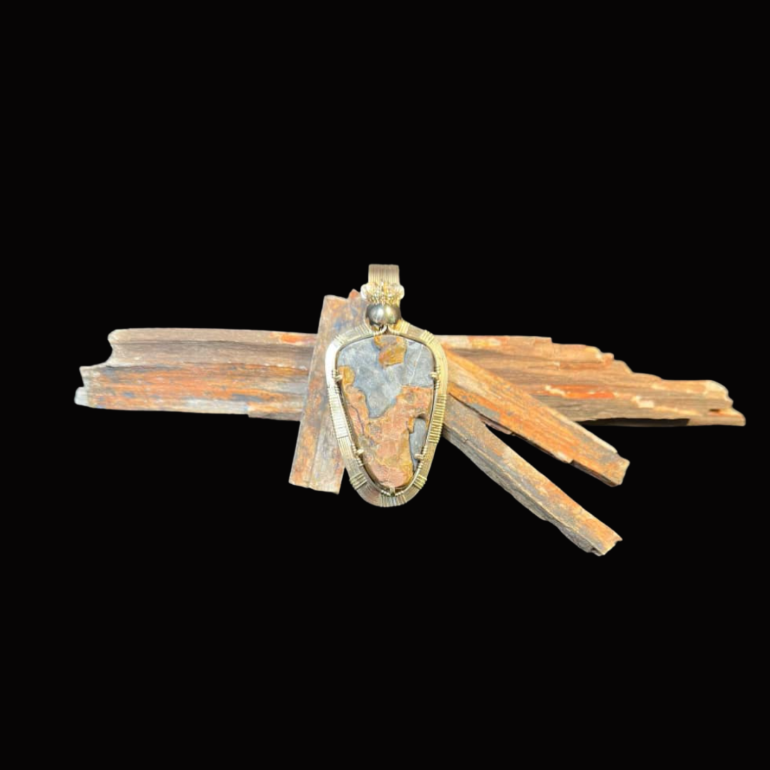 A silver pendant with a large gray stone, resting on a small pile of weathered, brown wooden sticks, against a black background.