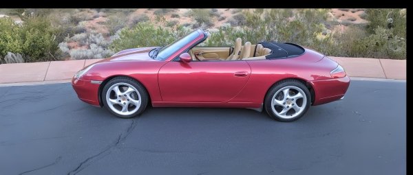 A shiny red convertible sits on black pavement in front of red rocks and sagebrush