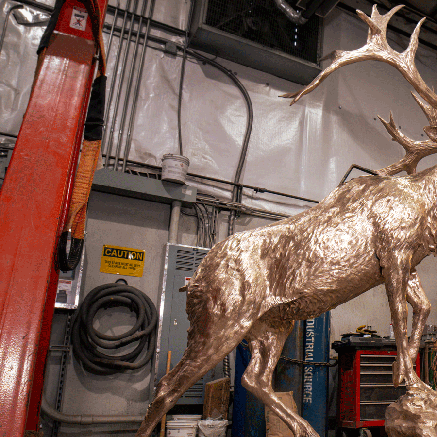 A large bronze elk sculpture with antlers in an industrial workshop.