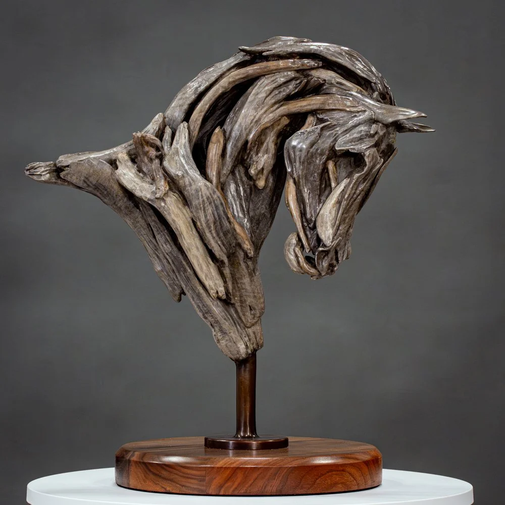A bronze sculpture of a horse's head made from layered driftwood with a wooden base.