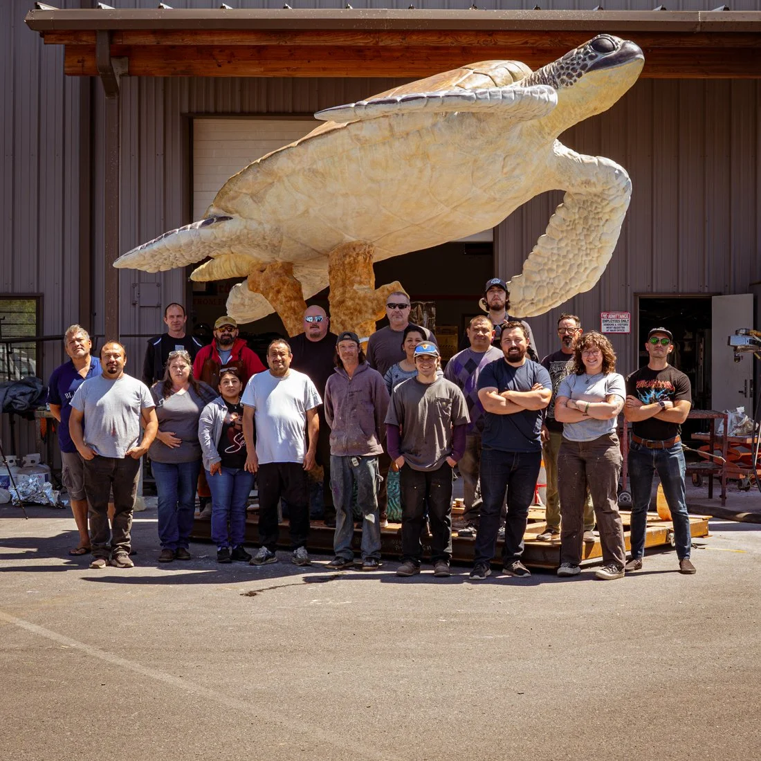 Group of people standing in front of a large turtle sculpture outside a building.