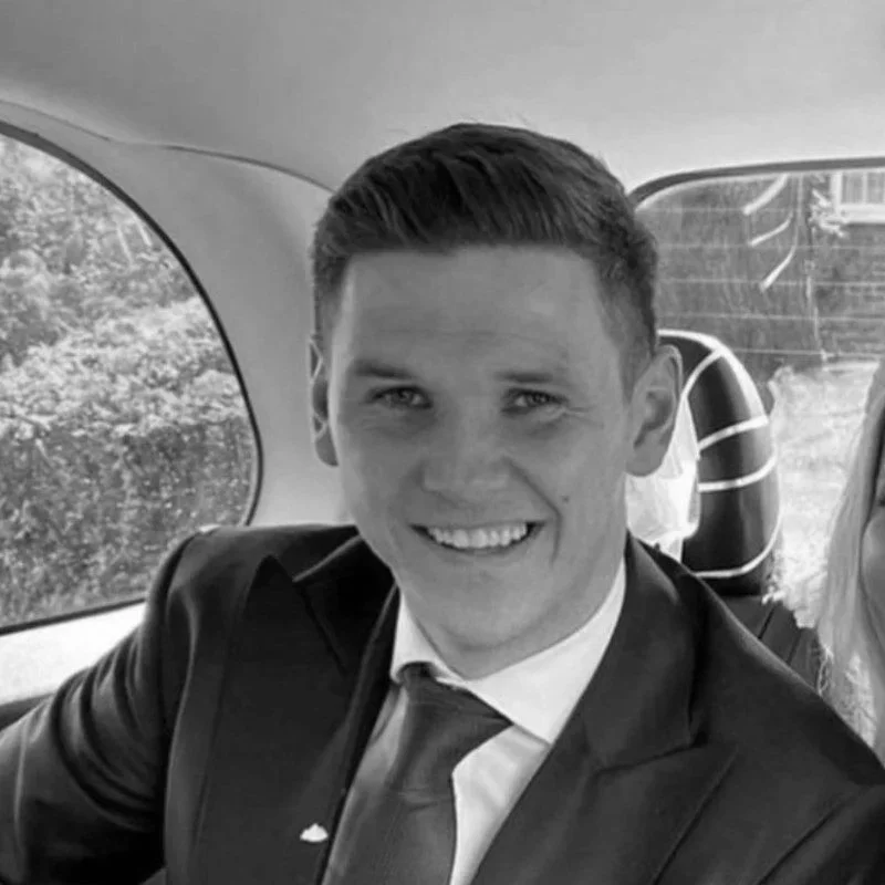 A smiling young man in formal attire sitting in the back seat of a car