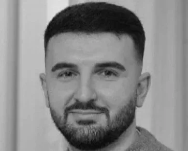 Black and white portrait of a man with short dark hair and a beard, looking at the camera.