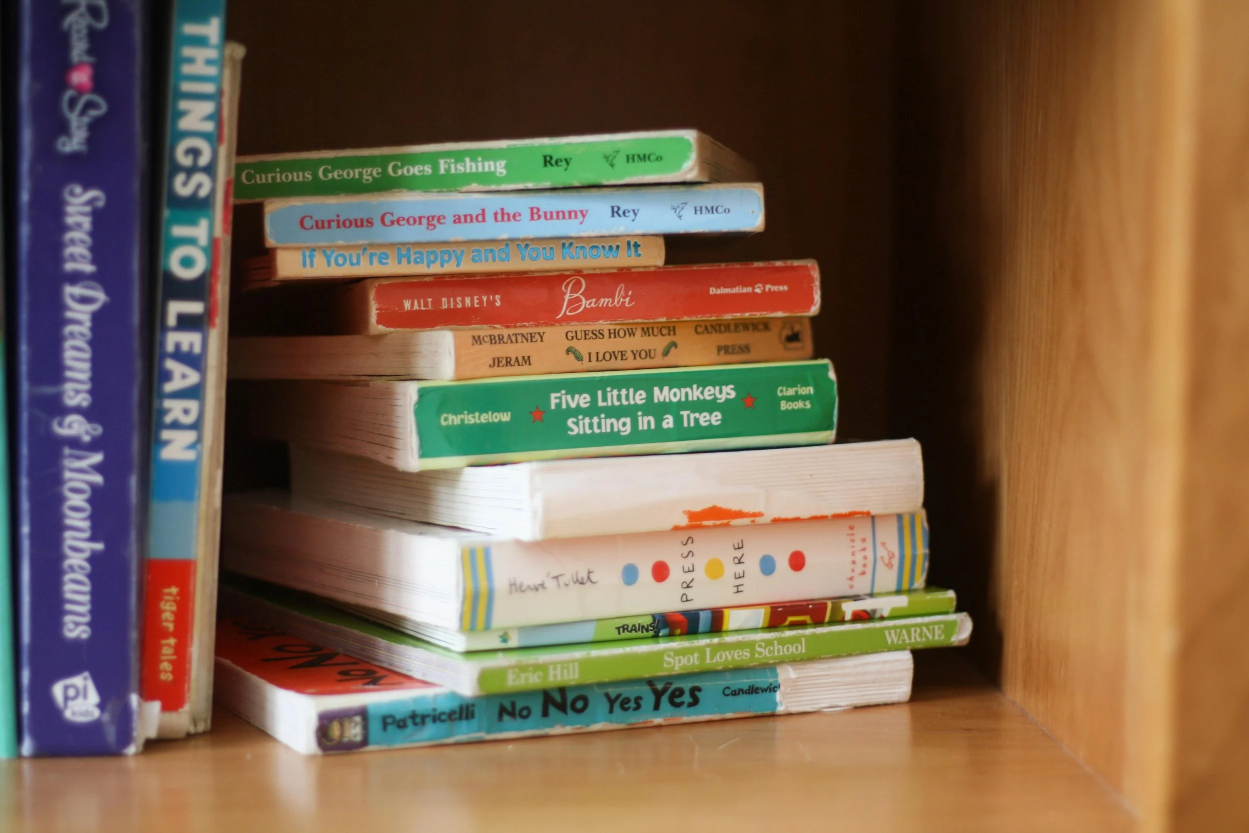 A stack of pre-loved children's books on a wooden bookshelf