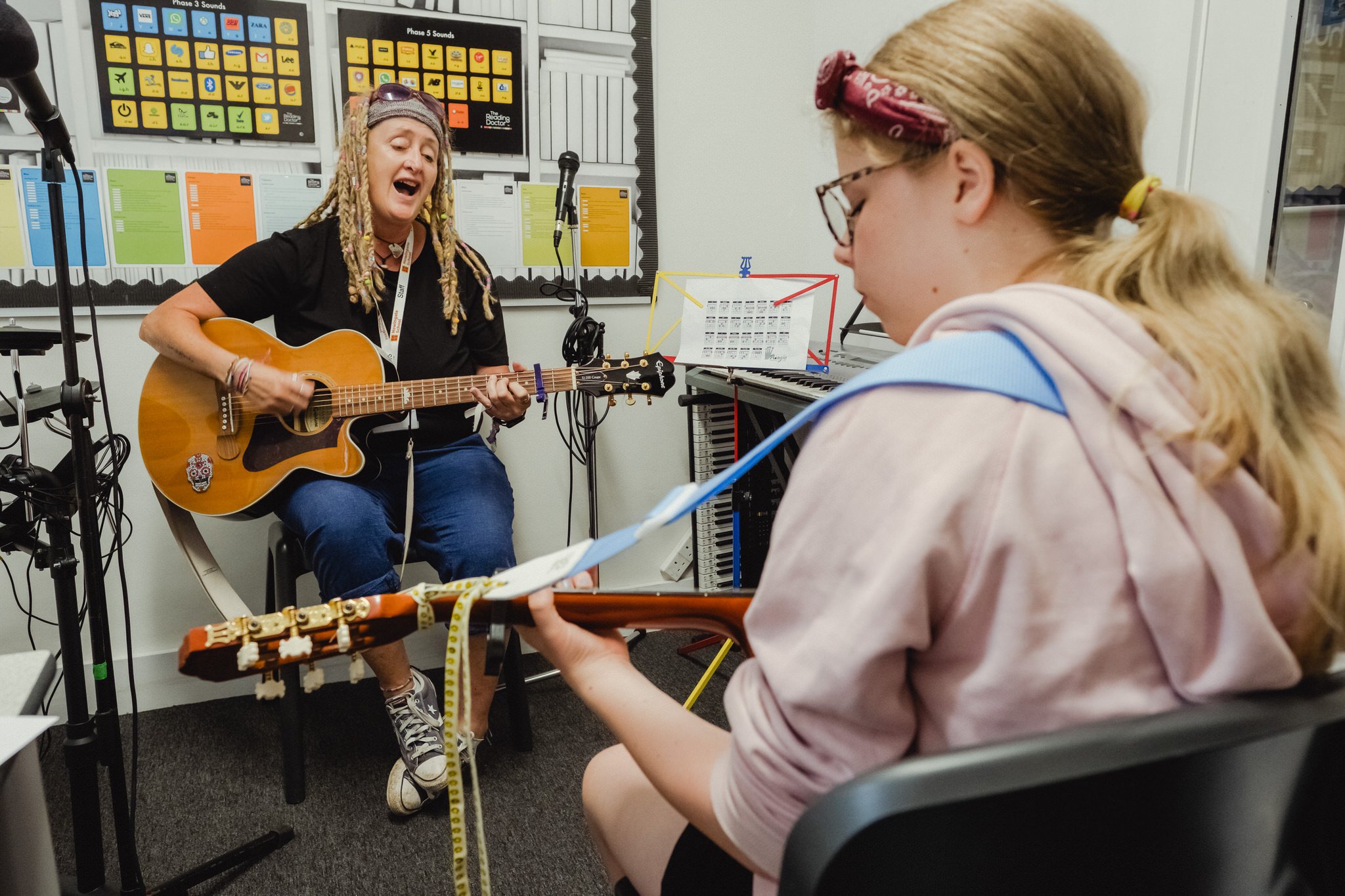 Student practicing guitar with her teacher in the music room