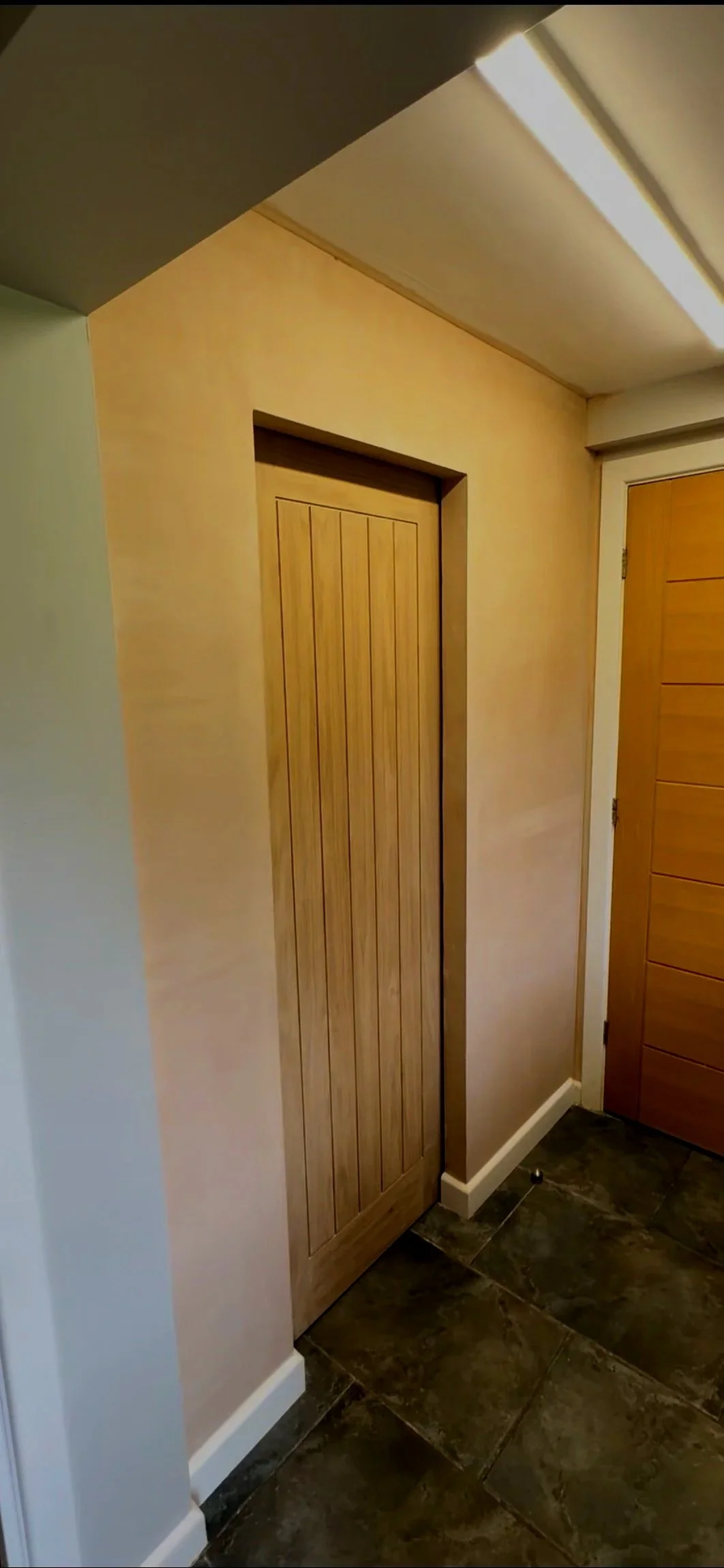 Interior view of a hallway with wooden doors, beige walls, and dark tiled flooring.