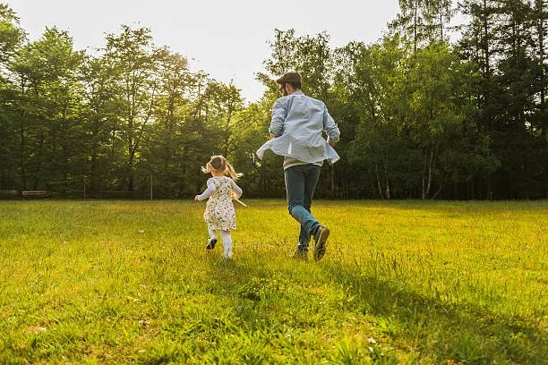 A child frolicking in an open field with her father.