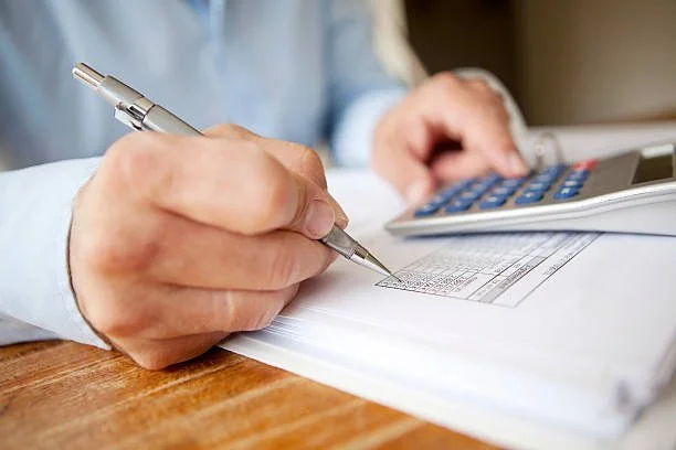 A man calculating personal expenses with pen, paper, and a calculator.