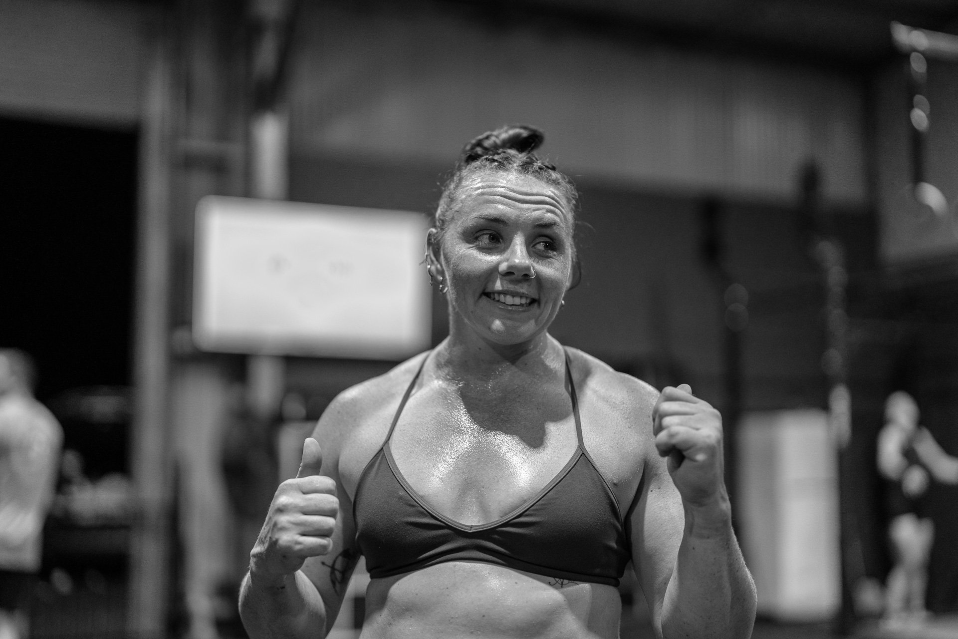Black and white photo of a woman smiling and holding her fists up in a boxing gym.