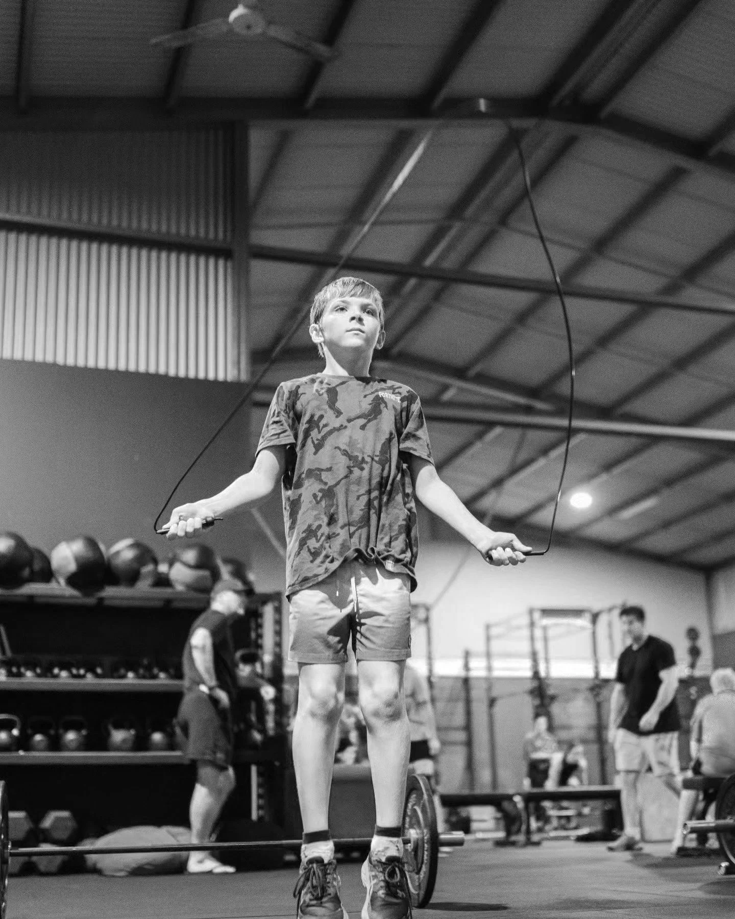 A young boy skipping rope in a gym, with weight racks and a punching bag in the background.