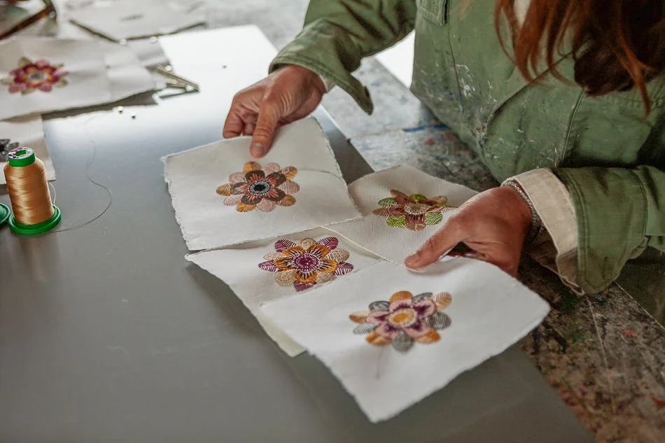 Dara Kay Barker examining embroidered fabric pieces with floral designs.