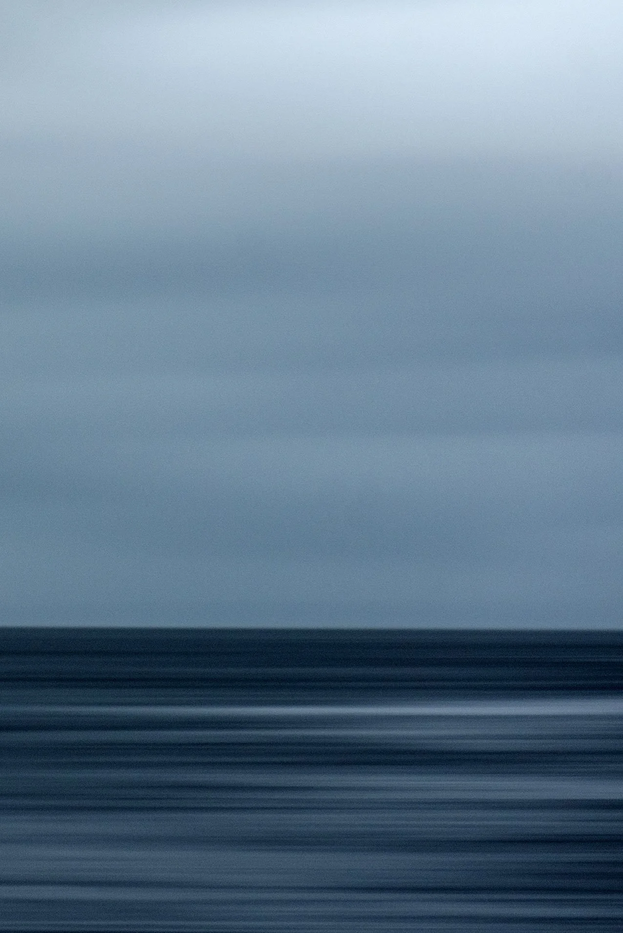 A long exposure photograph of the ocean at dusk, showing smooth, blurred water and a cloudy sky with a light blue hue.