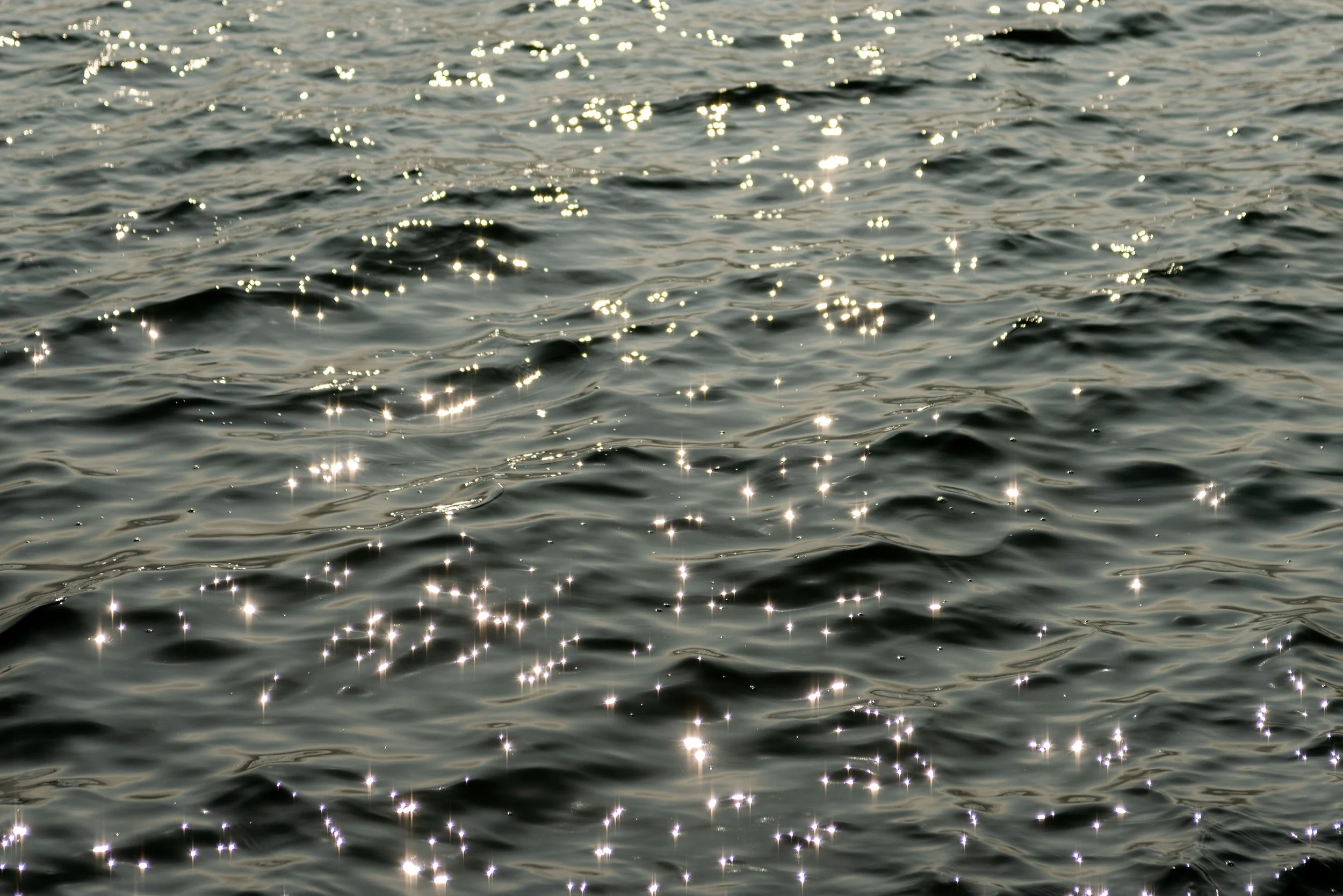Sunlight reflecting off the surface of dark ocean water, creating bright sparkling highlights.