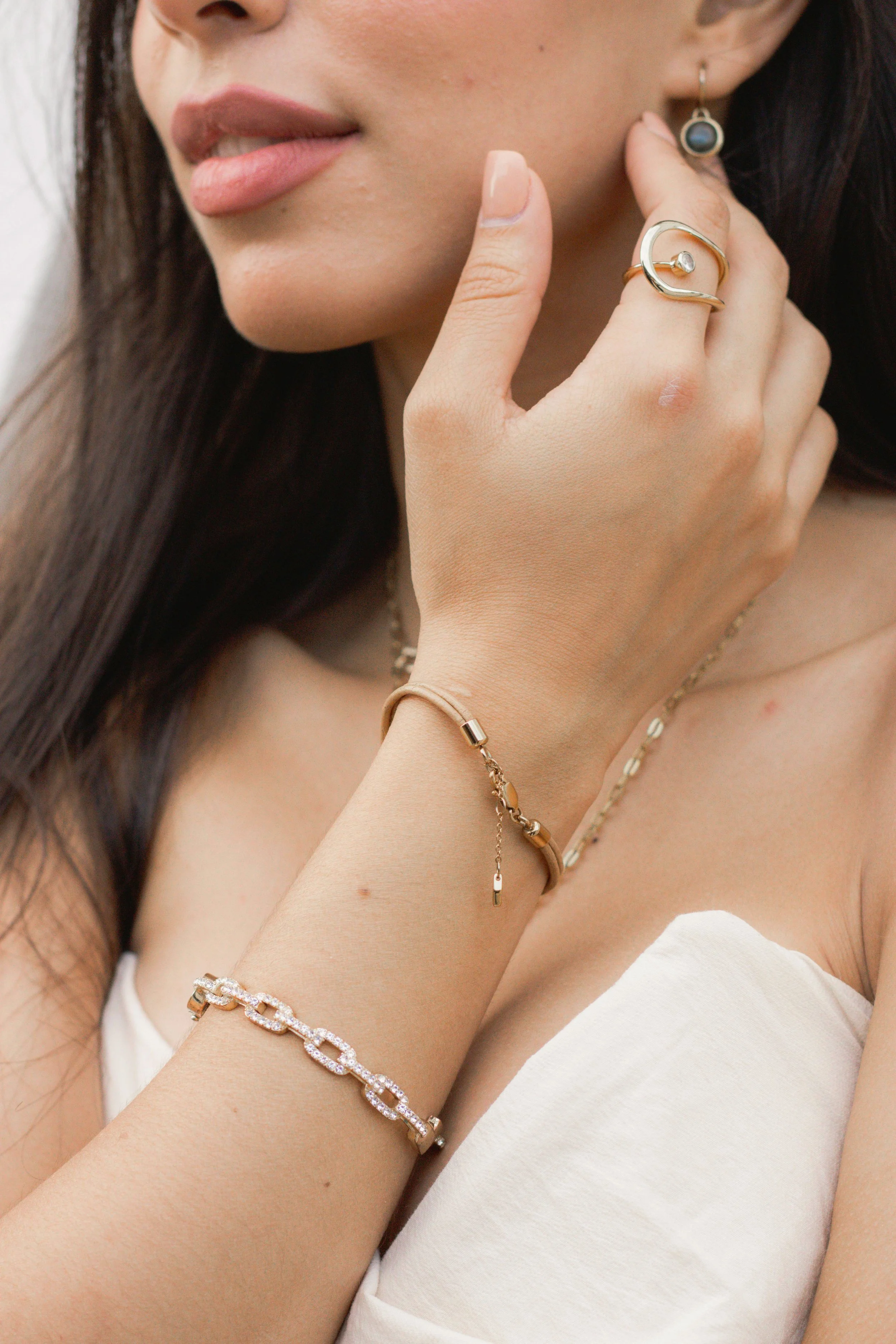 Close-up of a woman wearing gold jewelry, including rings, bracelets, a necklace, and earrings, with a focus on her lips and hand resting near her face.
