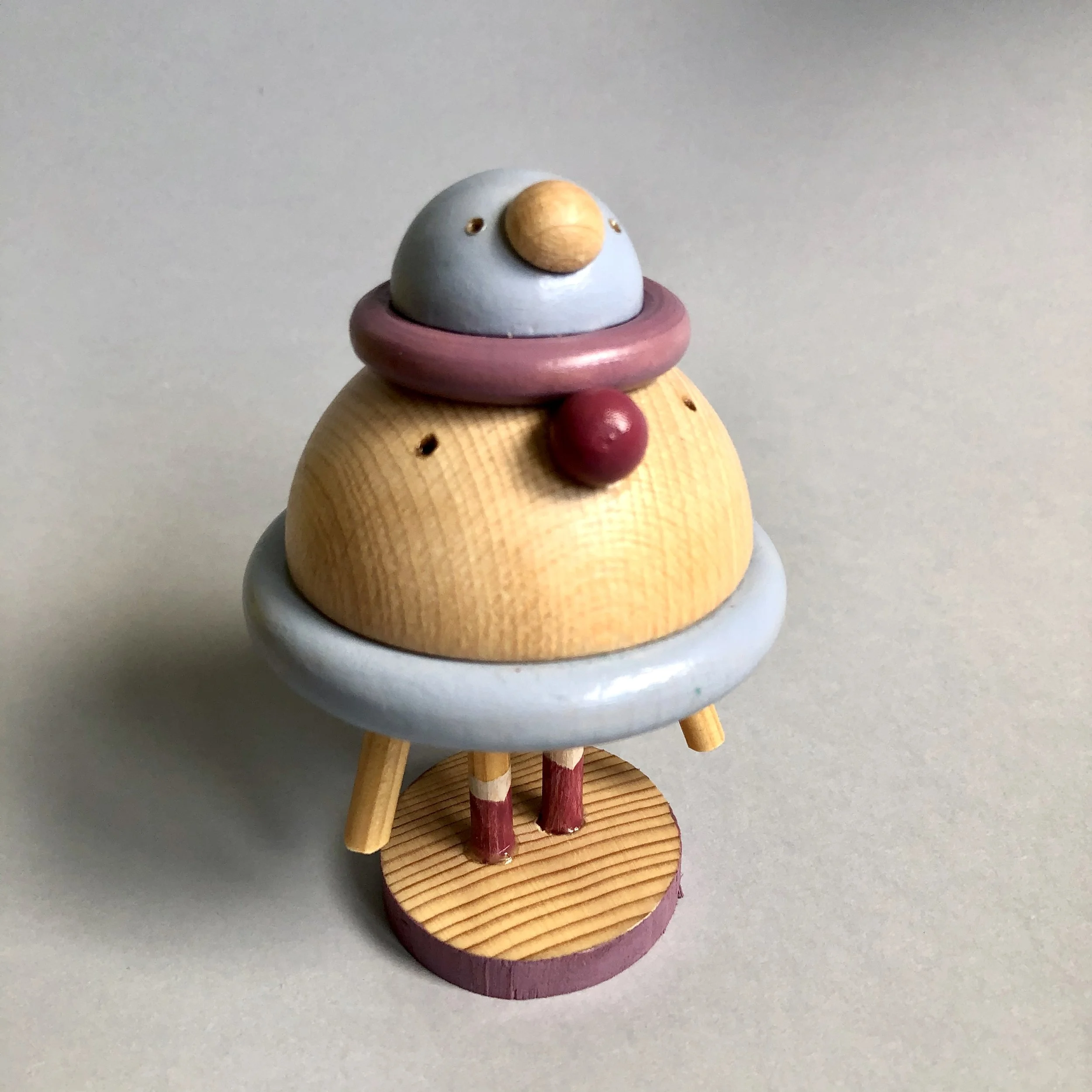 Handmade wooden toy figure resembling a bird, painted in pastel colors, standing on a wooden base.