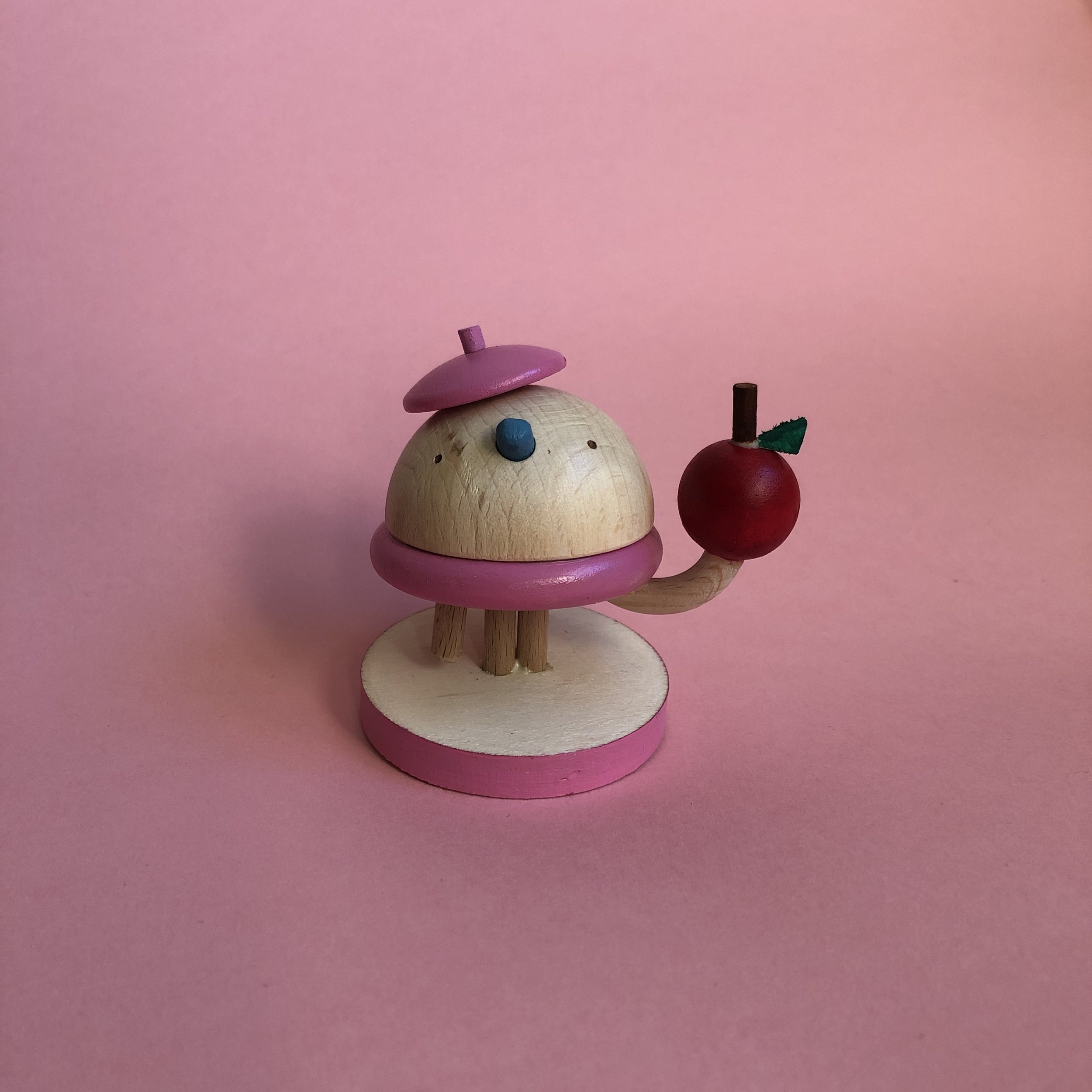 Close-up of small wooden figurines resembling animals, painted in pastel colors, against a pink background.