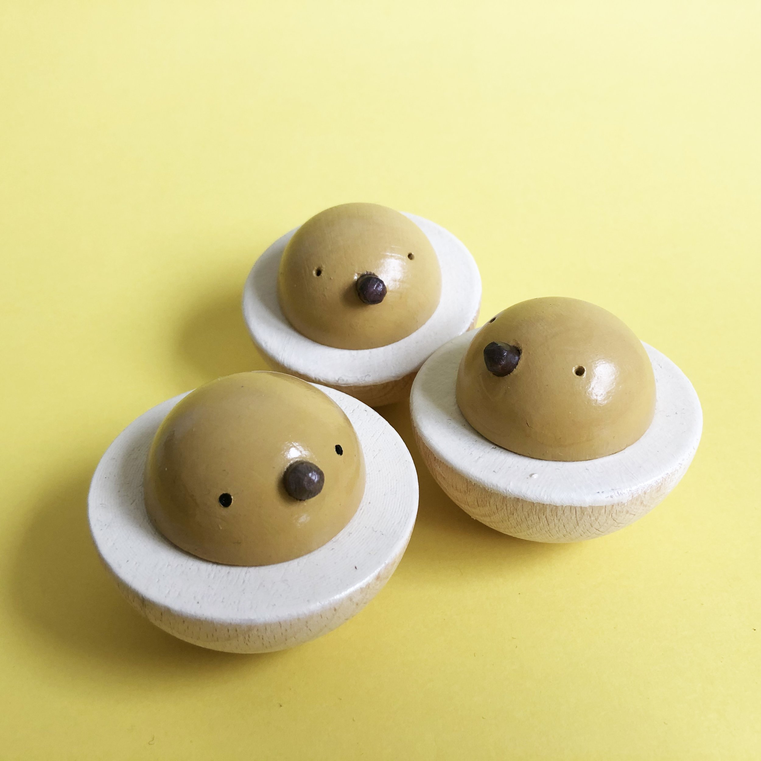 Close-up of a half-cut egg with a chick beak and eyes painted on the yolk, sitting on white egg whites against a yellow background.