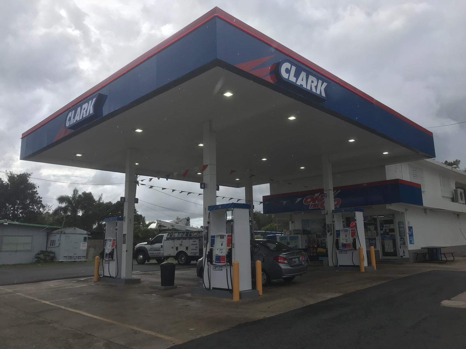 Una estación de servicio Clarks con surtidores de gasolina y un coche estacionado, en un día nublado.