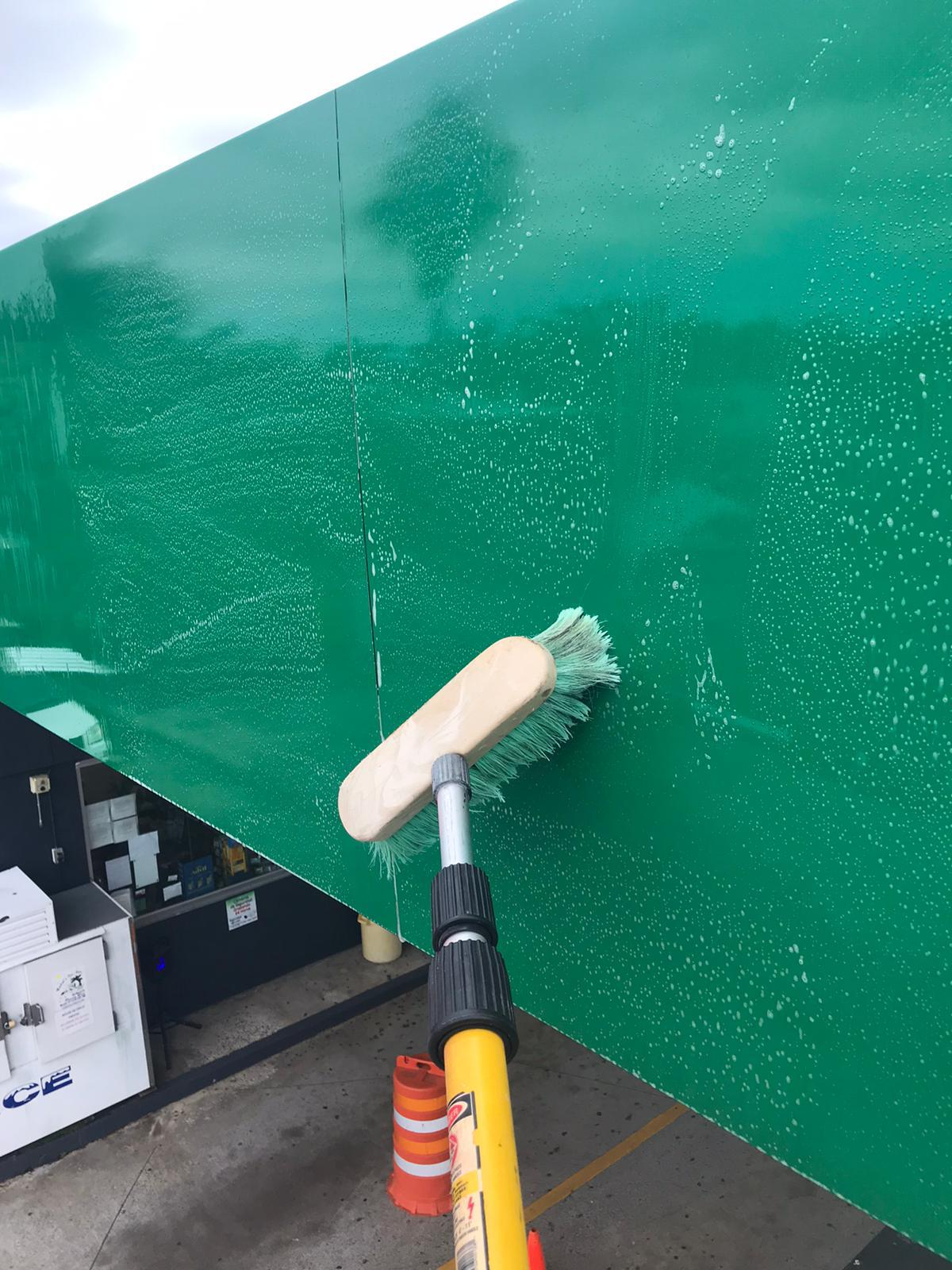 Lavando una fachada de color verde con un cepillo giratorio en un área de estacionamiento.