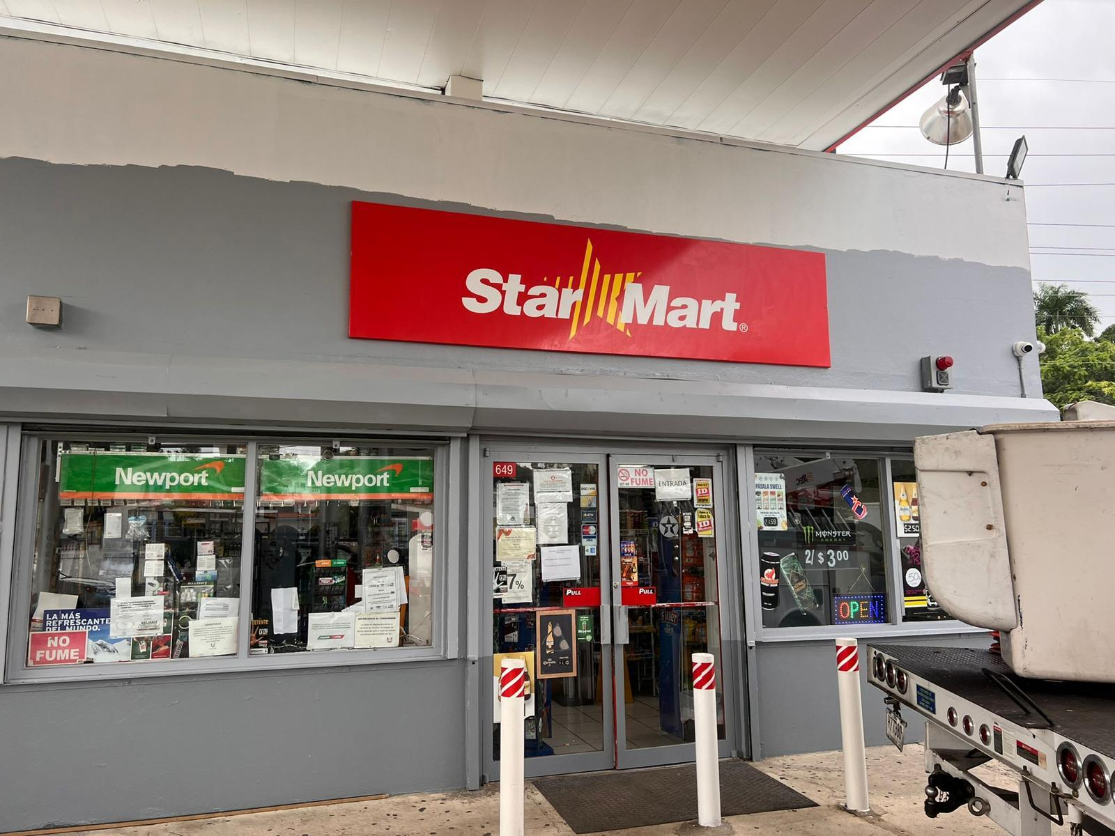 Fachada de una tienda de conveniencia llamada Star Mart con anuncios en las ventanas y una señal de abierto en la ventana.