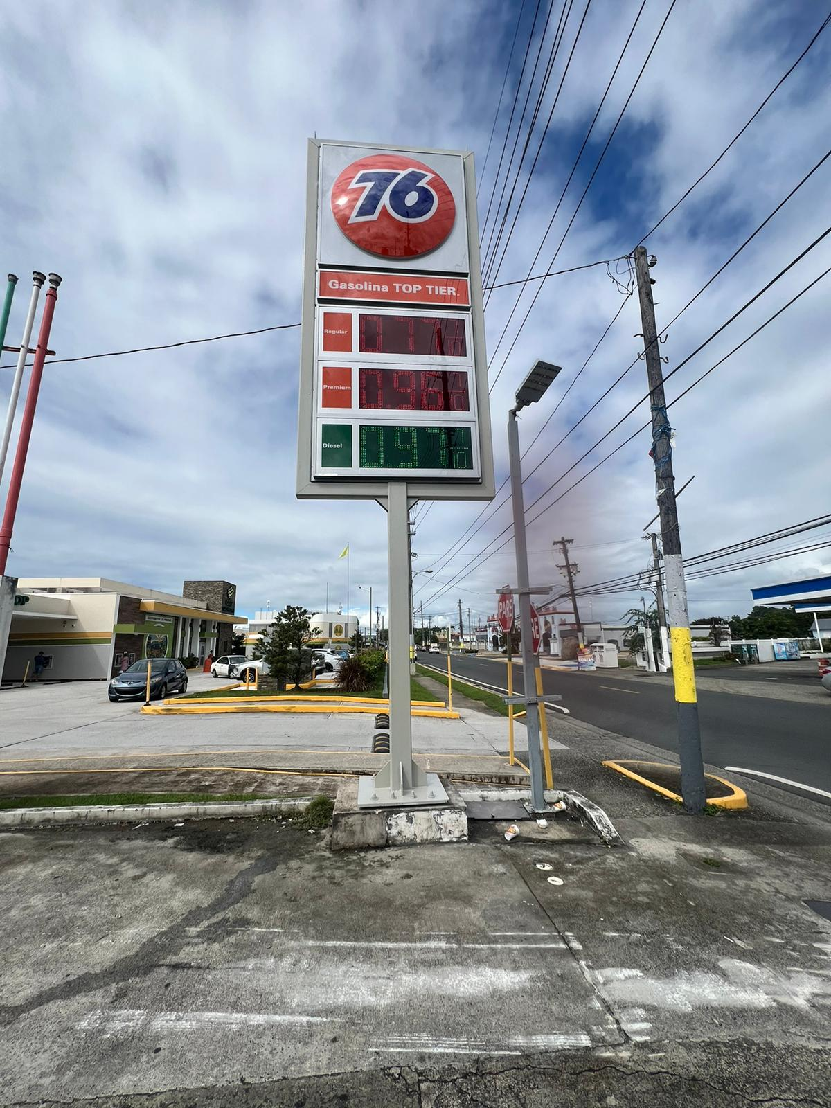 Cartelera de gasolina en una estación de servicio mostrando los precios para gasolina regular, premium y diésel en un día con cielo parcialmente nublado.