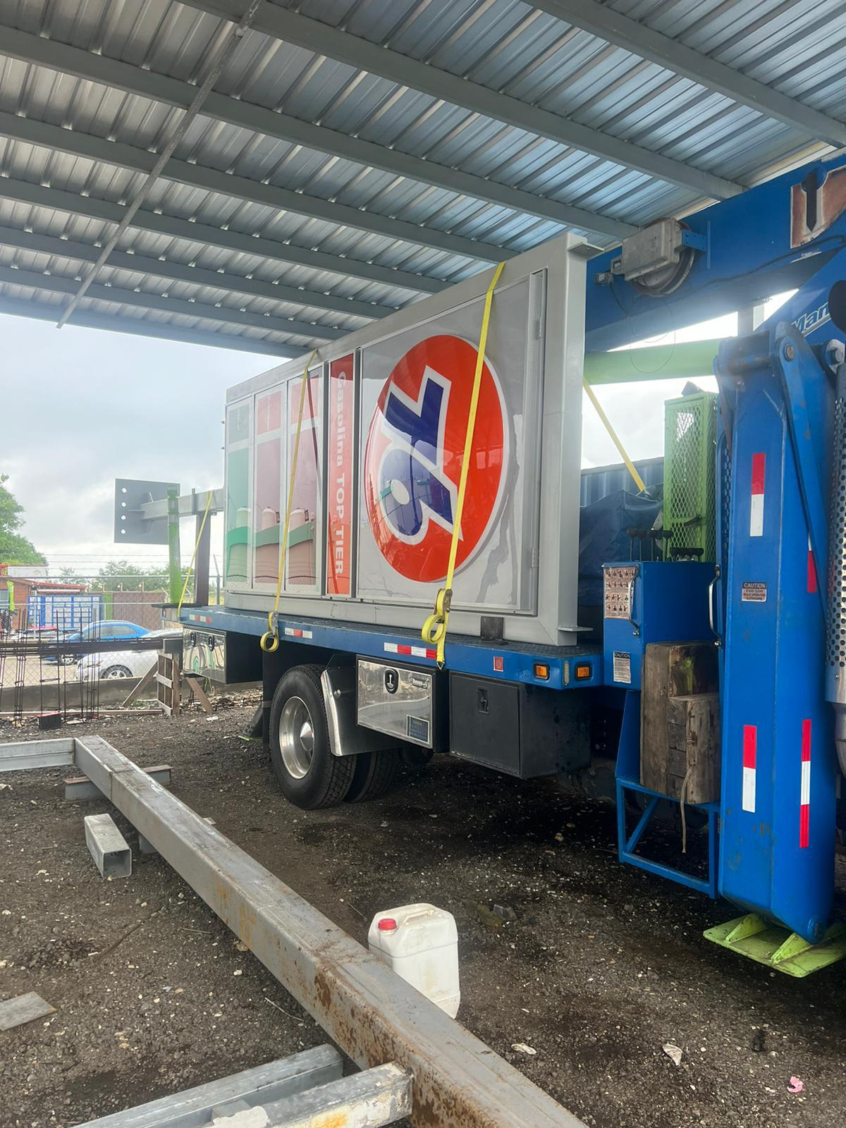 Camión de comida con logo de 7-Eleven estacionado bajo un techo metálico, con herramientas y equipo de construcción alrededor.
