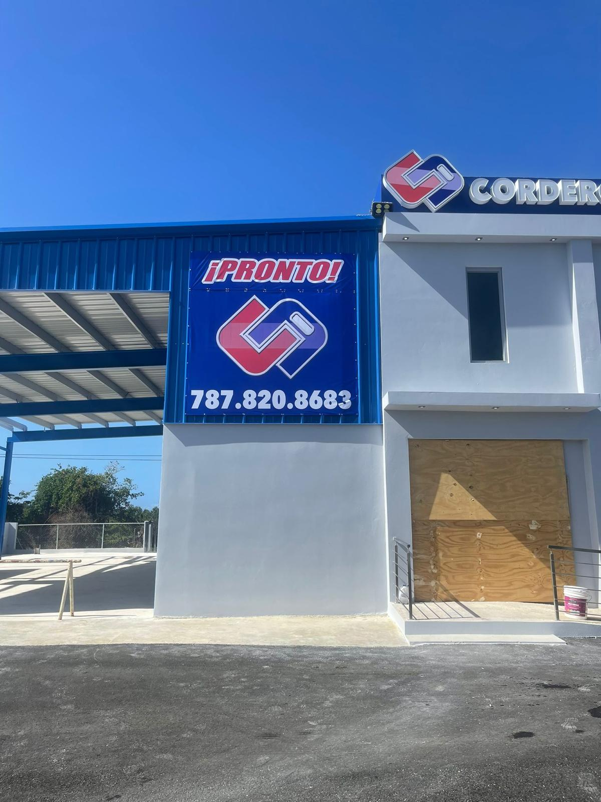 Fachada de un establecimiento con un cartel grande azul que tiene el logo de Cordero y el texto ¡Pronto! junto con un número de teléfono. El nombre Cordero también aparece en un letrero en la parte superior del edificio.