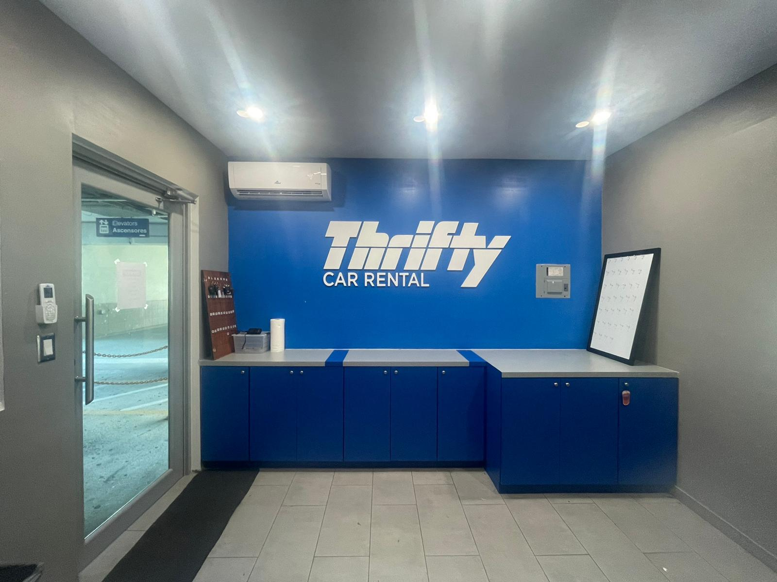 Mostrador de recepción en un local de alquiler de autos con un fondo azul que dice 'Thrifty Car Rental'.