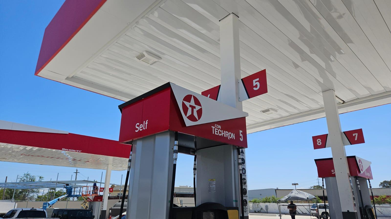 Estación de servicio con bombas de gasolina, señalización y un cielo despejado.