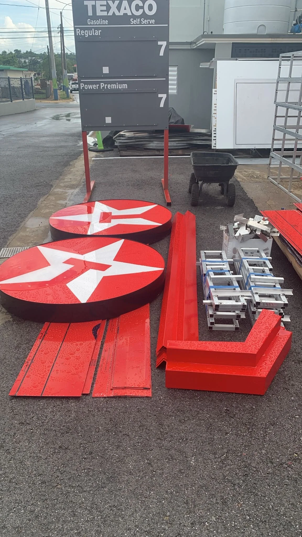 Letreros y componentes para una estación de servicio Texaco, incluyendo un letrero con los precios de gasolina, piezas metálicas y estructuras de señalización en proceso de montaje.